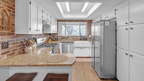 A modern kitchen with white cabinets, a brick accent wall, and a large island with a granite countertop. - Dean's Retreat At Georgetown 3 Bedroom Home (Georgetown)