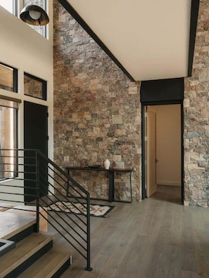 Ein modernes Interieur mit einer Steinsäule, einer Treppe mit schwarzen Geländern und einem Holzboden.