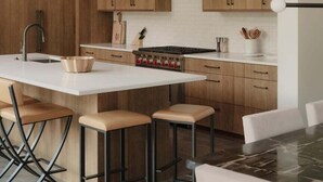 A modern kitchen with wooden cabinets, a central island with stools, pendant lighting, and a stainless steel sink. - 8 Speedwell 4 Bedroom Home (Big Sky)