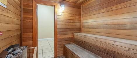 Een sauna met houten wanden en banken, een betegelde vloer en een deur naar een andere ruimte.