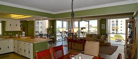 A spacious living area with a dining table, chairs, a sofa, and a kitchen in the background.