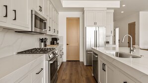 A modern kitchen with white cabinetry, stainless steel appliances, and a wooden floor. - Pearl Beach B 3 Bedroom Townhouse (St. George)