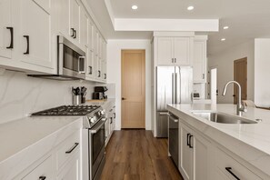 A modern kitchen with white cabinetry, stainless steel appliances, and a wooden floor. - Pearl Beach B 3 Bedroom Townhouse (St. George)