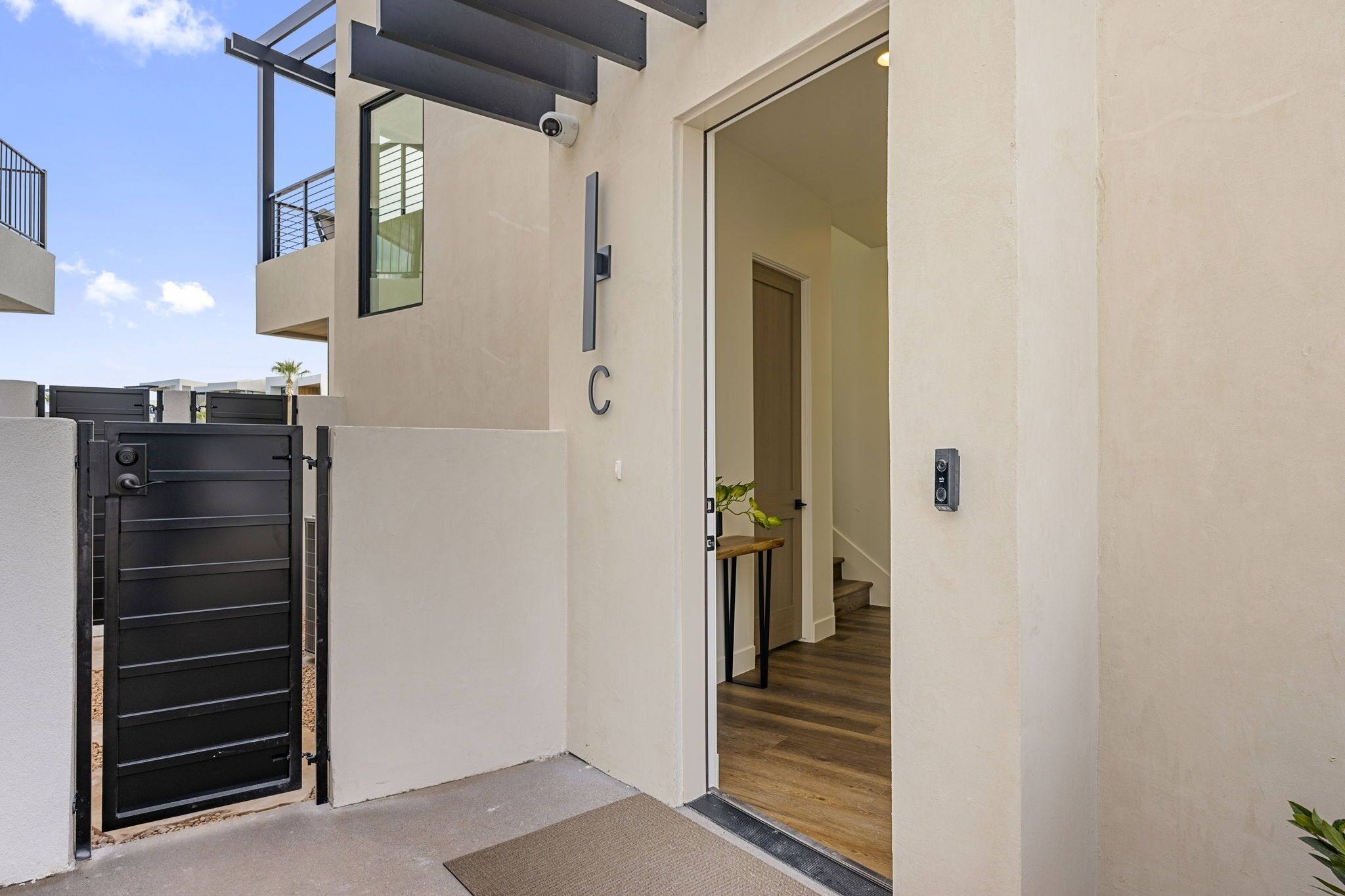 Ein moderner Hauseingang mit schwarzem Gitter, einer Treppe, die zu einer oberen Etage führt, und einem kleinen Tisch mit einer Pflanze.