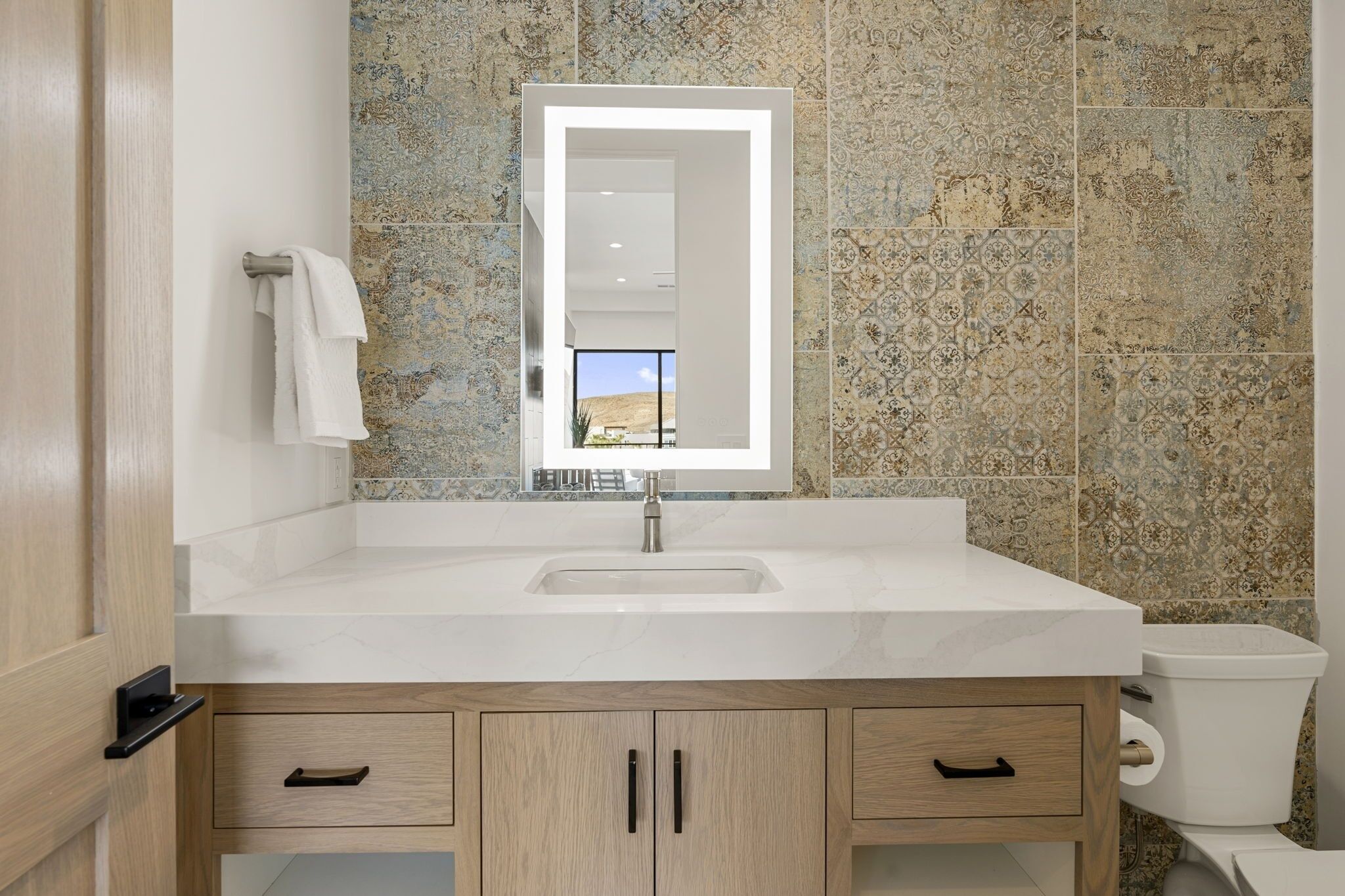 Un baño moderno con un espejo grande, un lavabo blanco y un inodoro.