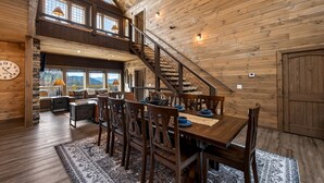 A spacious dining area with a wooden table and chairs, a staircase, and a view of the outdoors. - Skywalk 5 Bedroom Home (Sevierville)