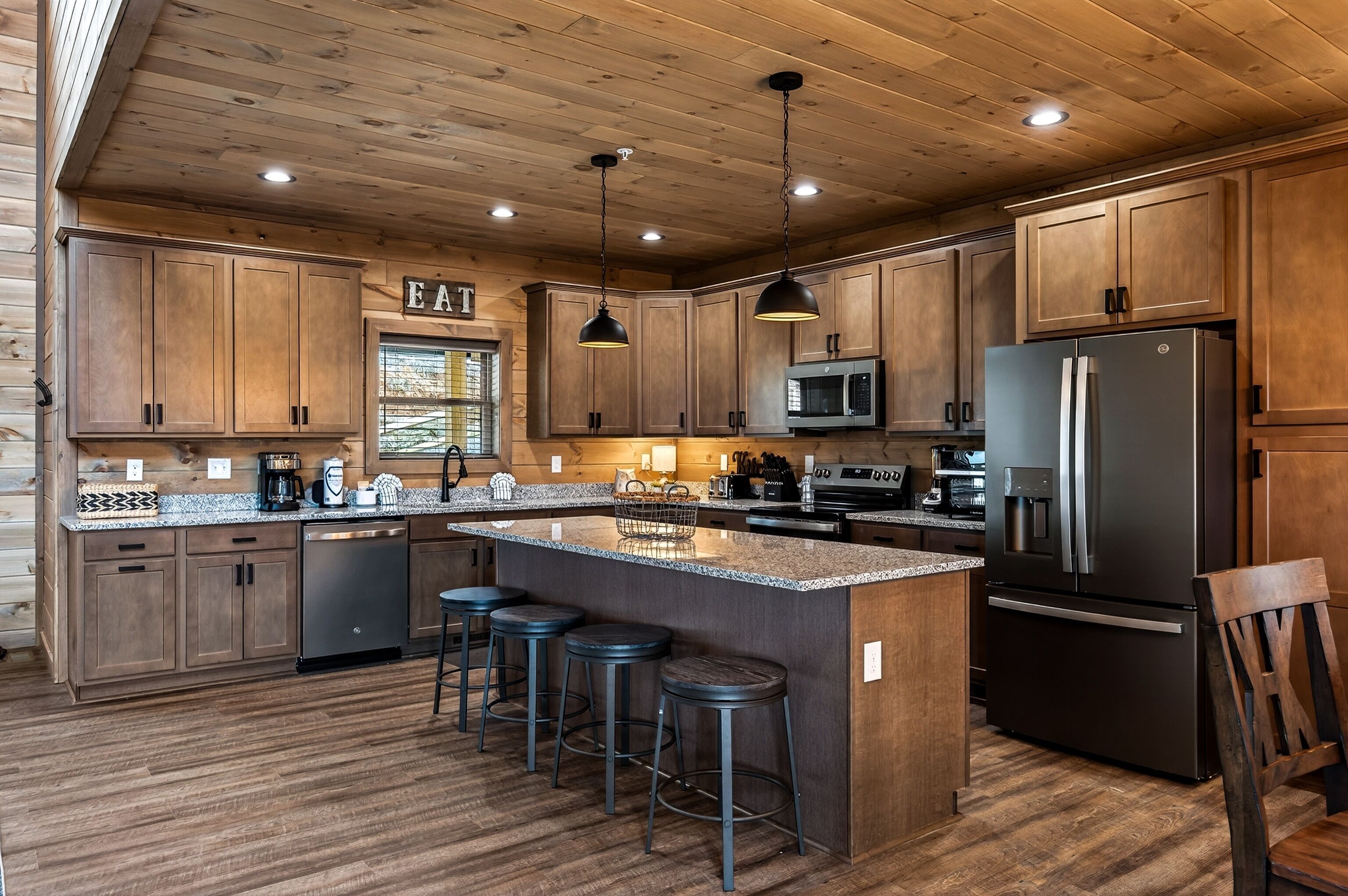 Une cuisine moderne avec des meubles en bois, un îlot central doté de tabourets, des appareils en acier inoxydable et un éclairage suspendu.