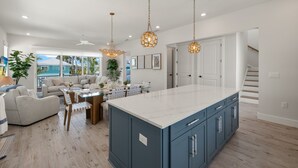 A spacious living area with a large island, a dining table, and a sofa. There are pendant lights, a ceiling fan, and a view of the outdoors. - 5583 Sun & Salt Retreat: 5br/4.5ba New Pool Home! 5 Bedroom Home (Fort Myers Beach)