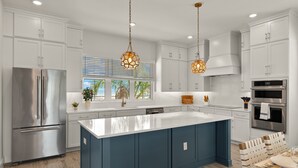 A modern kitchen with white cabinets, a large island, stainless steel appliances, and pendant lighting. - 5583 Sun & Salt Retreat: 5br/4.5ba New Pool Home! 5 Bedroom Home (Fort Myers Beach)