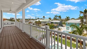 A wooden deck with a white railing, overlooking a residential area with houses and a swimming pool. - 5583 Sun & Salt Retreat: 5br/4.5ba New Pool Home! 5 Bedroom Home (Fort Myers Beach)