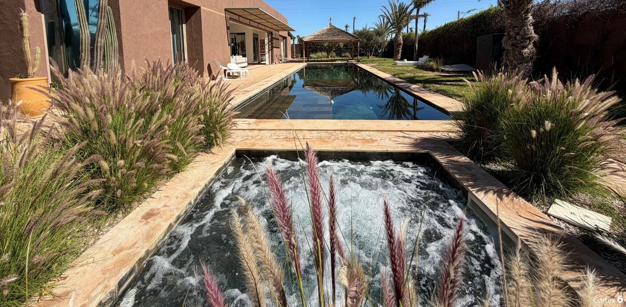 Piscina con caída de agua rodeada de zonas ajardinadas y un edificio con terraza.