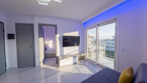 Ein modernes Wohnzimmer mit einem großen Schiebeglastür zum Balkon, einem wandmontierten Flachbildfernseher und einem minimalistischen Design mit Marmorboden.
