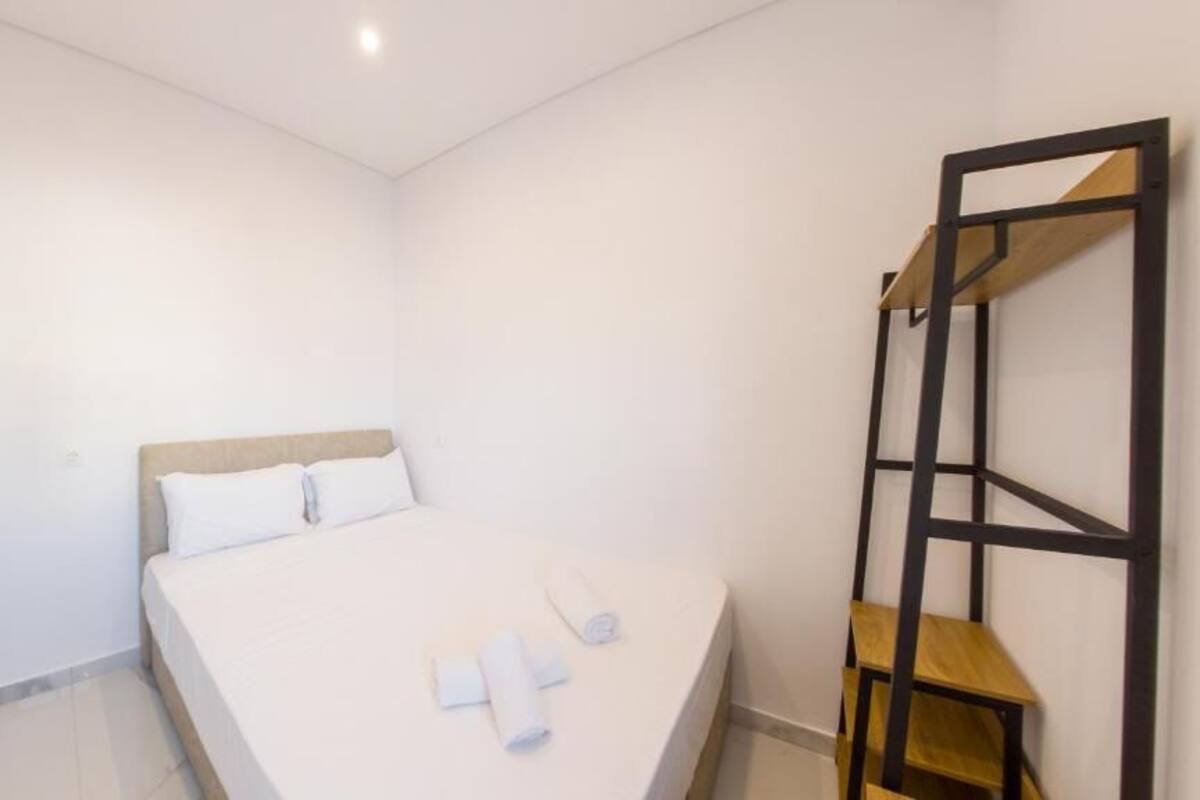 Habitació petita i neta, amb un llit, una estantària de fusta i una porta.