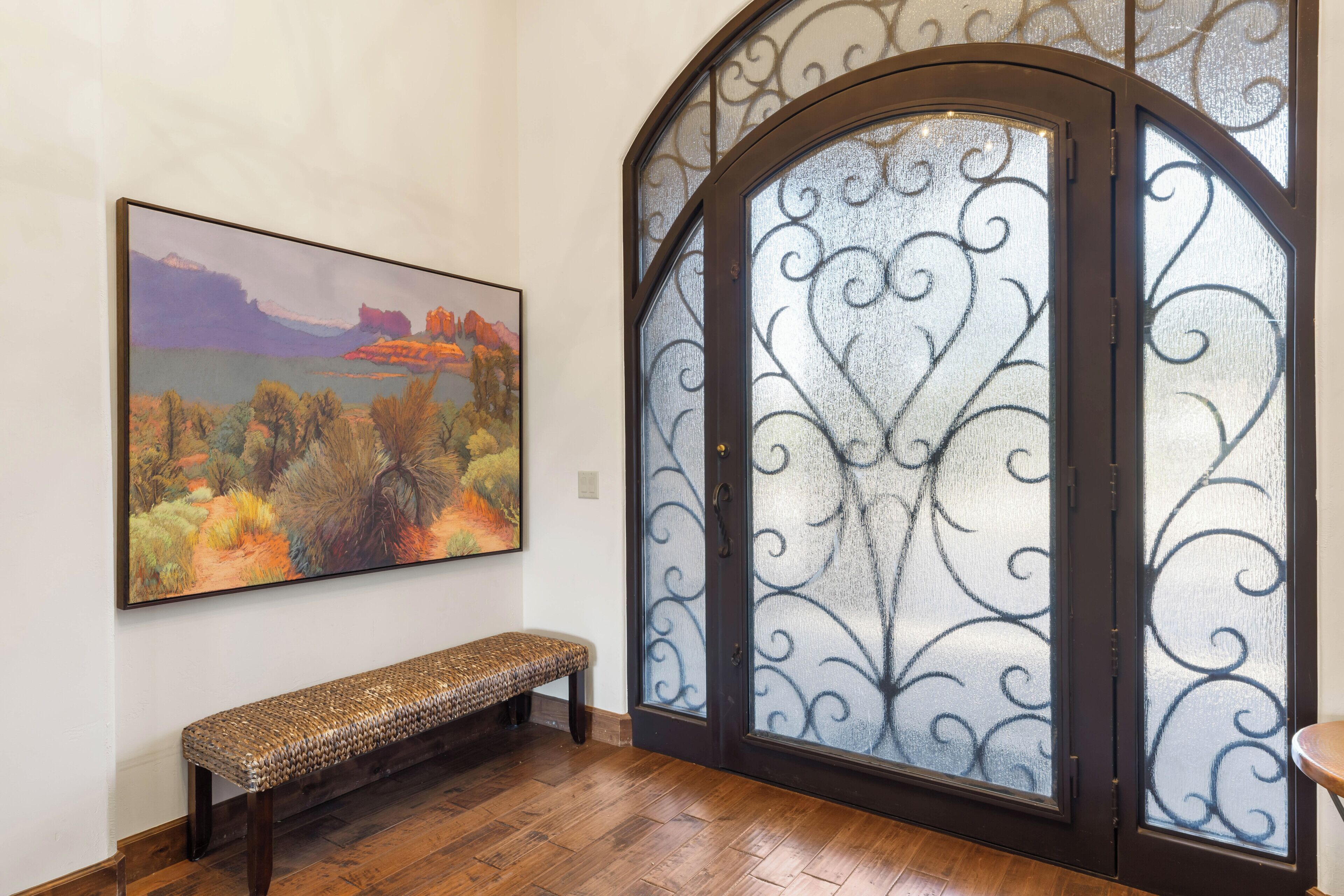 A room with a wooden bench, a painting of a landscape, and a decorative glass door.