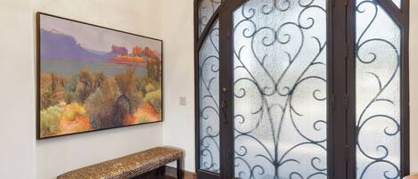 A room with a wooden bench, a painting of a landscape, and a decorative glass door.