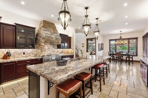 A kitchen with granite countertops, a stone fireplace, and bar stools.