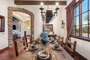 A dining area with a long wooden table, stone archway, and a chandelier.