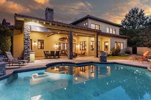 A two-story house with a swimming pool, stone pillars, and outdoor seating.