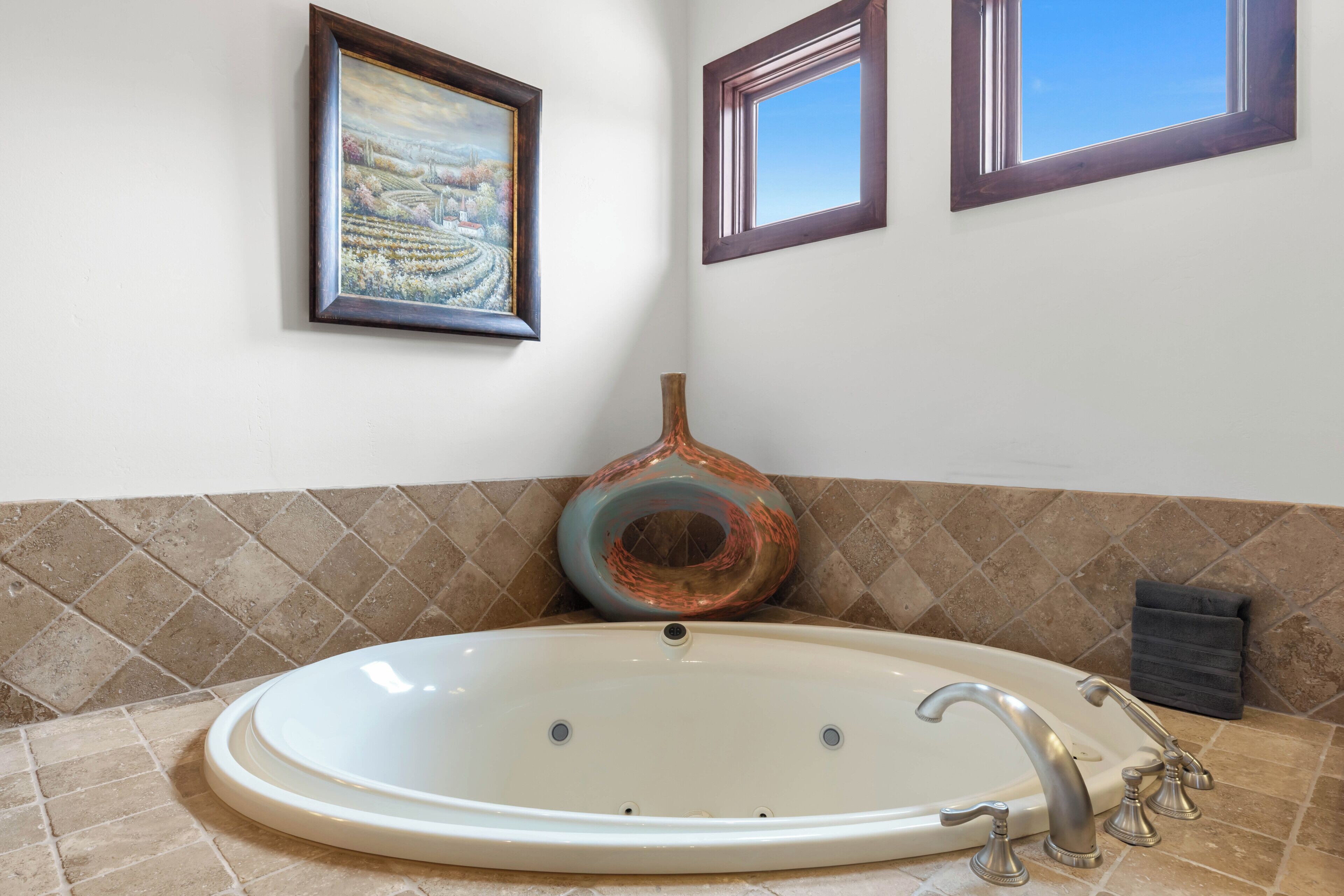 Ein Badezimmer mit einer großen Badewanne, einer Vase und zwei gerahmten Bildern an der Wand.