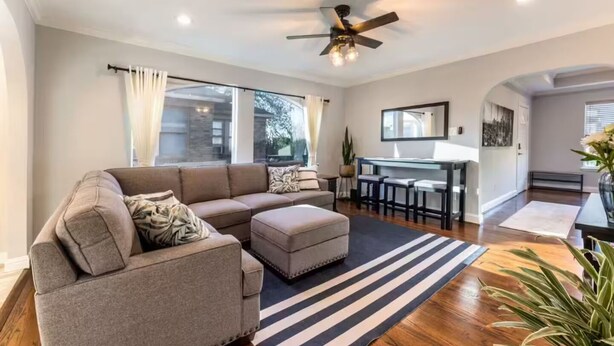 A modern living room with a sectional sofa, a dining area with a glass table, and a ceiling fan. - Entire Property_Charming House_Museum District (Houston)