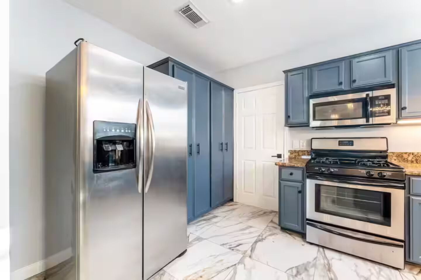 A modern kitchen with stainless steel appliances, blue cabinets, and a marble floor.