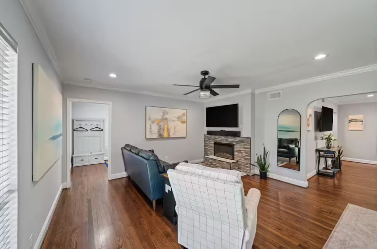 A spacious living room with hardwood flooring, a blue sofa, a white armchair, a fireplace, and a ceiling fan.