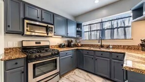 A modern kitchen with dark cabinets, stainless steel appliances, granite countertops, and a window with a view of trees. - Entire Property_Charming House_Museum District (Houston)
