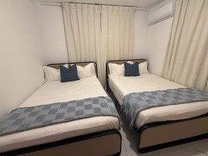 Zwei Einzelbetten mit Kopfteilen, weiße Bettwäsche und eine blaue Decke.