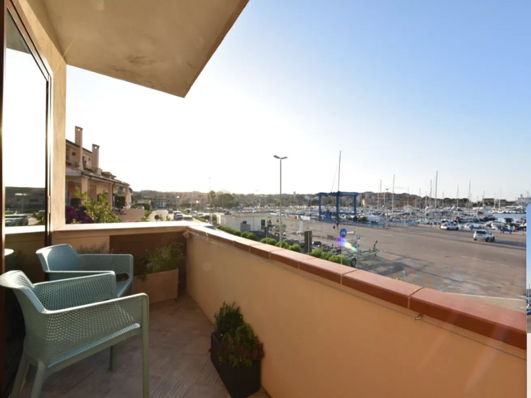 Un balcon avec deux fauteuils en osier, une plante en pot et une vue sur une marina avec des bateaux et un parking.
