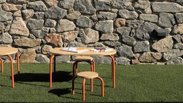 A table with chairs and a notepad on a grassy area, with a stone wall in the background.