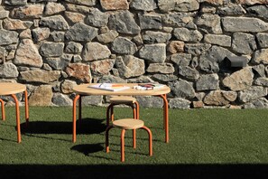 A table with chairs and a notepad on a grassy area, with a stone wall in the background. - Neme Slow Living Retreat (Rethymno)