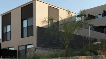 A modern building with a stone wall in the foreground, large windows, and a flat roof.