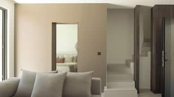 A modern living room with a sofa, a staircase, and a door leading to another room.
