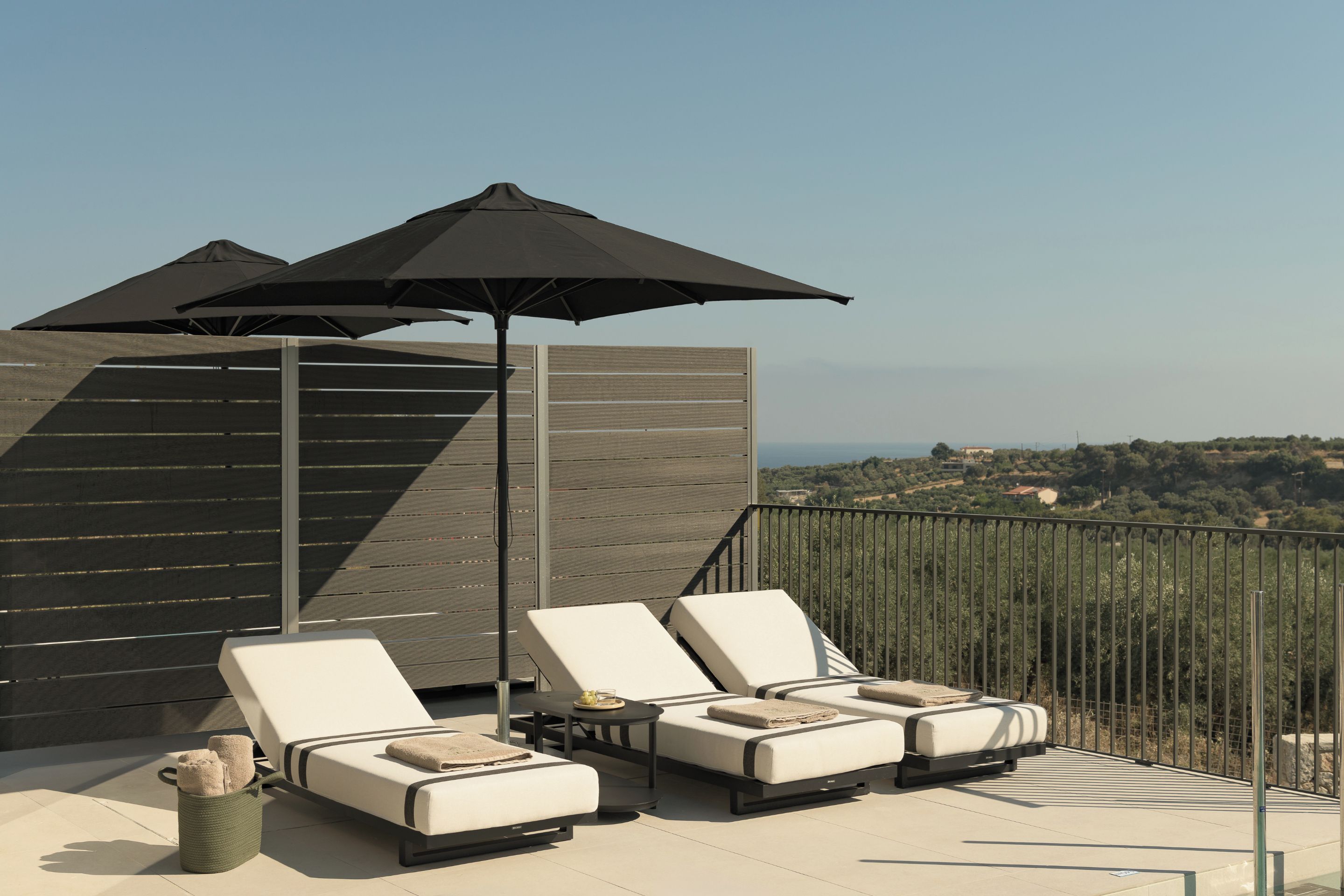 Une terrasse avec deux fauteuils, une table et deux parasols.