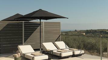 Une terrasse avec deux fauteuils, une table et deux parasols.