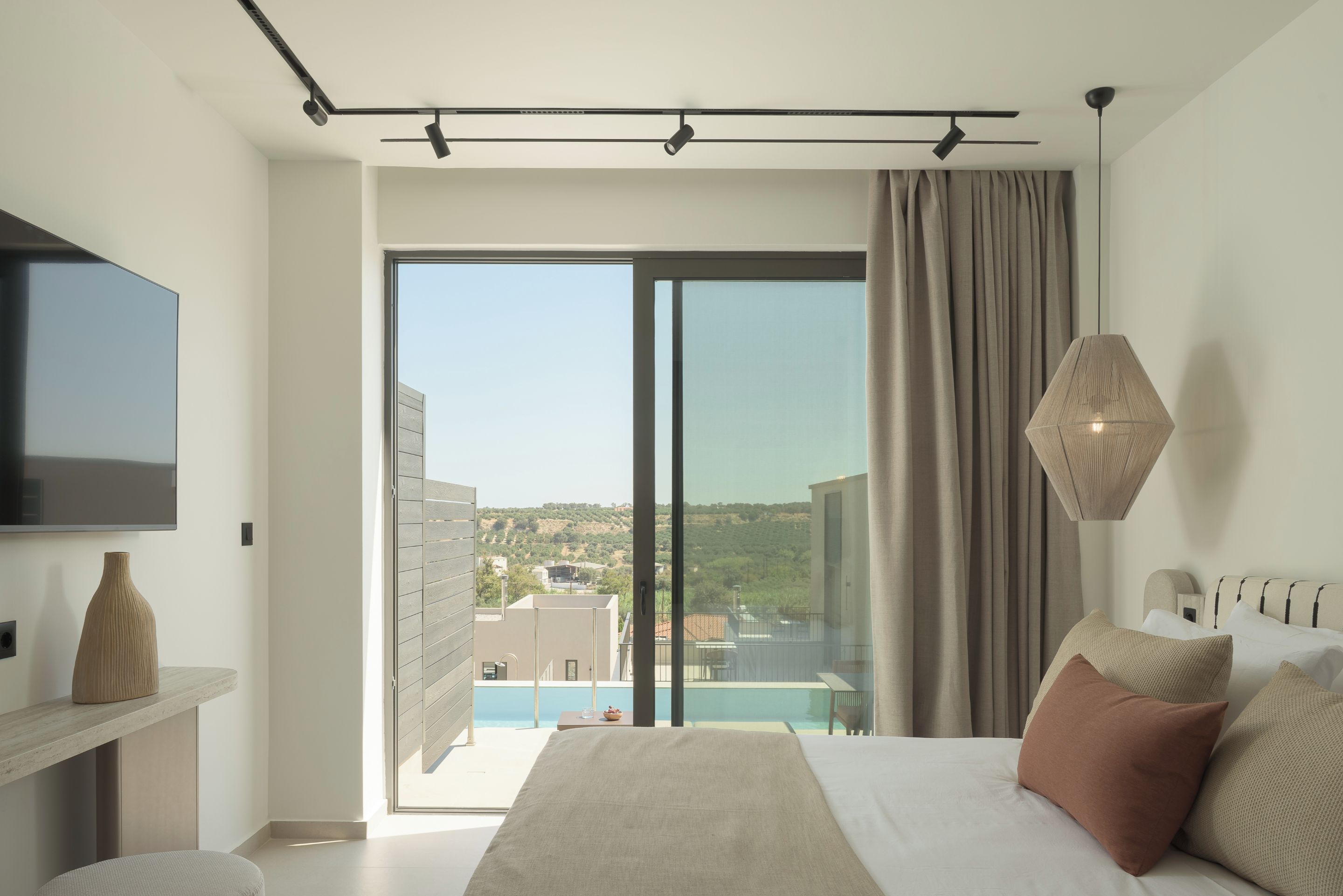 Un dormitorio moderno con una cama grande, un televisor de pantalla plana, vista a una piscina y un balcón.