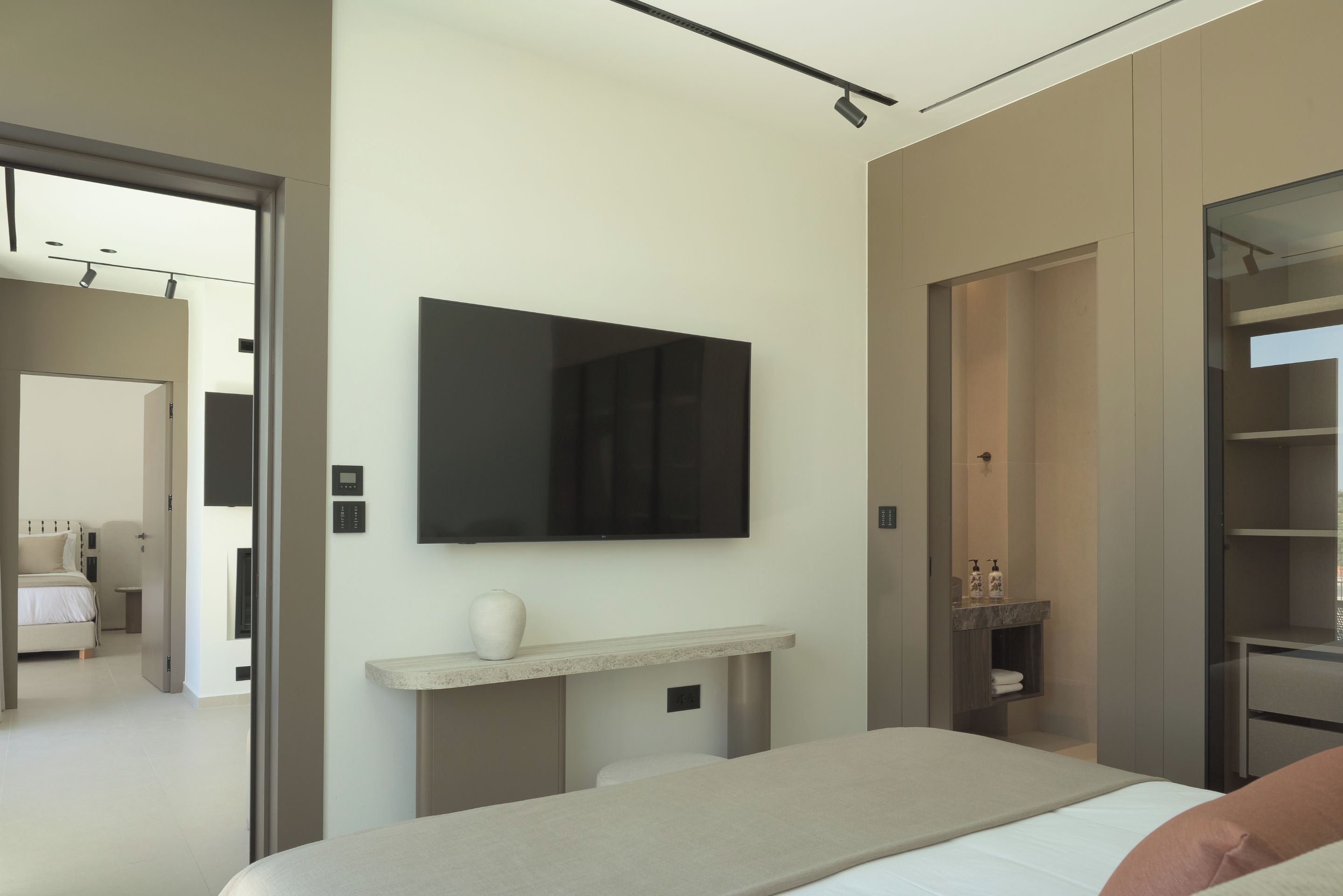 A modern hotel room with a bed, a mounted TV, a small console table, and a wardrobe.
