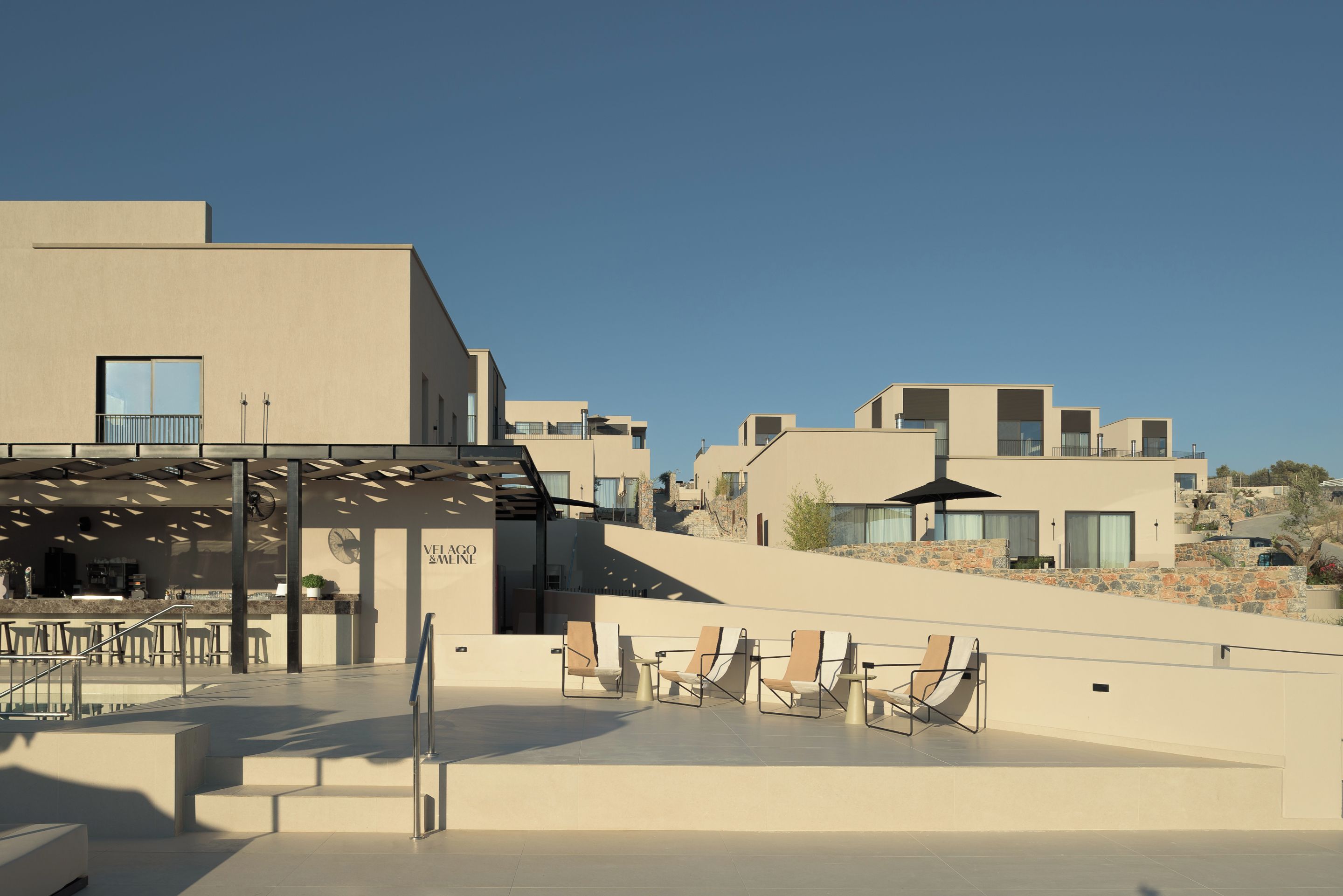 A modern building with a flat roof, a bar area with outdoor seating, and a clear sky.