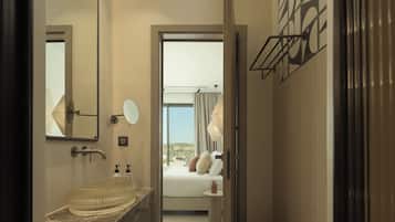 Une salle de bain moderne avec un lavabo en verre, un grand miroir et une vue sur une chambre à coucher avec un lit et une fenêtre.