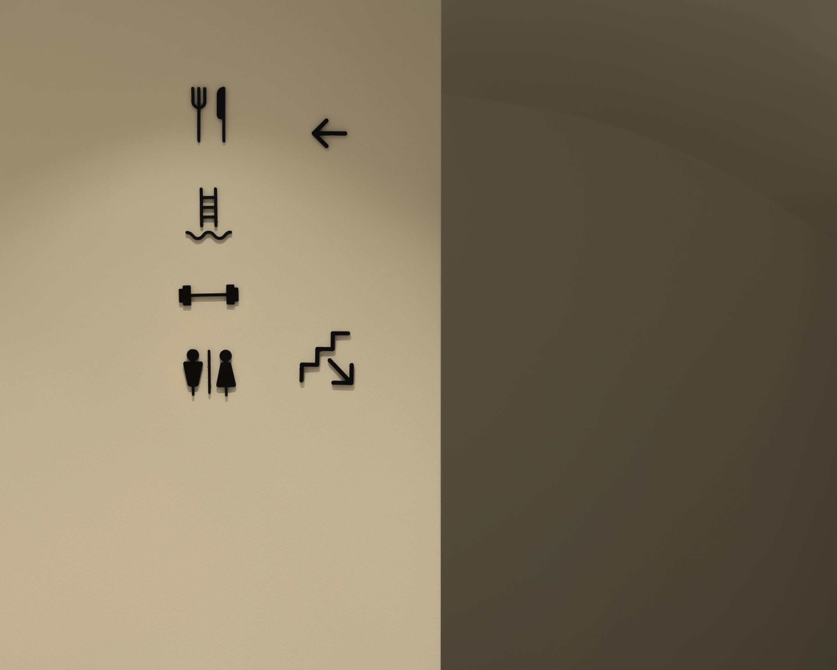 A wall with icons indicating a dining area, a pool, a gym, and a staircase.