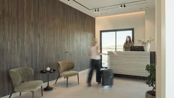 Una zona de recepción moderna con pared de madera, dos sillones tapizados, una mesita con un libro y una planta en maceta.