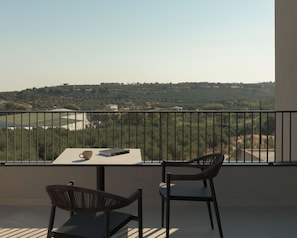Un balcon avec une table et deux chaises, donnant sur un paysage vallonné.