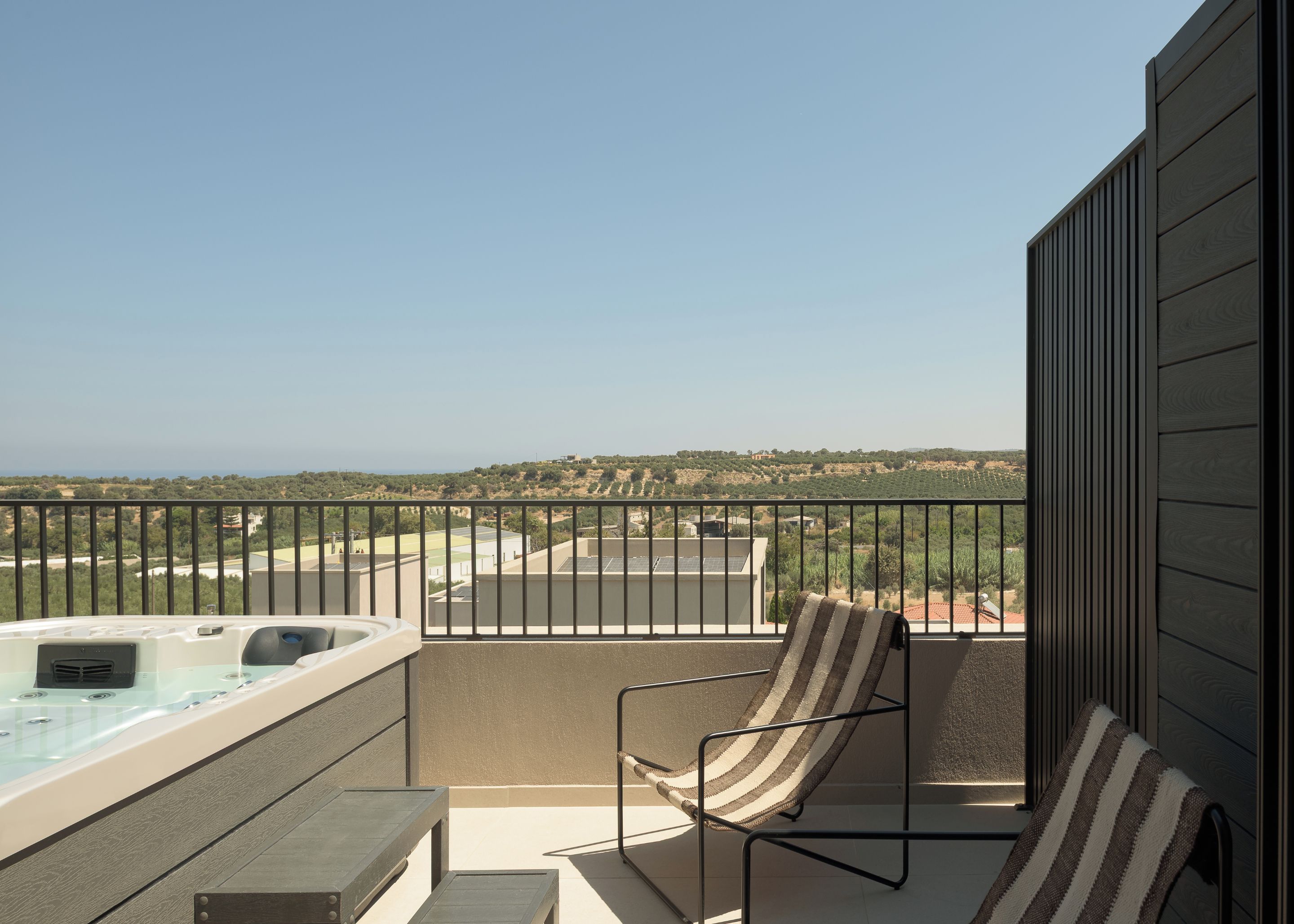 Un balcón con un jacuzzi, una silla a rayas y vistas a un paisaje montañoso.