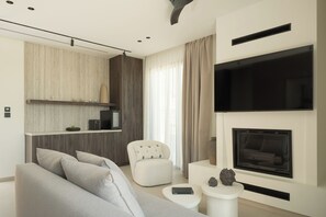 A modern living room with a sofa, armchair, fireplace, television, and a small side table. - Neme Slow Living Retreat (Rethymno)
