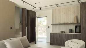 A modern living room with a sofa, a chair, a wooden cabinet, and a stone wall. - Neme Slow Living Retreat (Rethymno)
