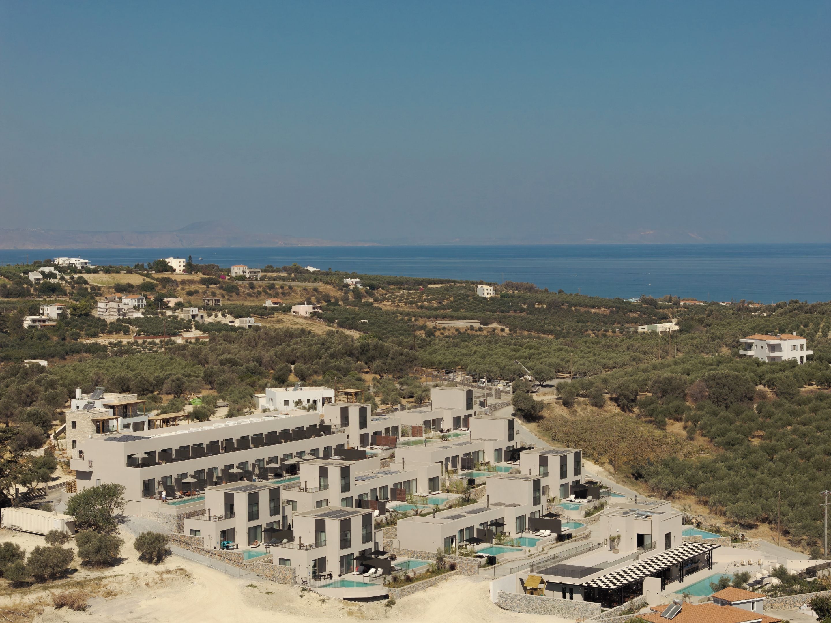 A modern resort with multiple buildings, a swimming pool, and a view of the sea.