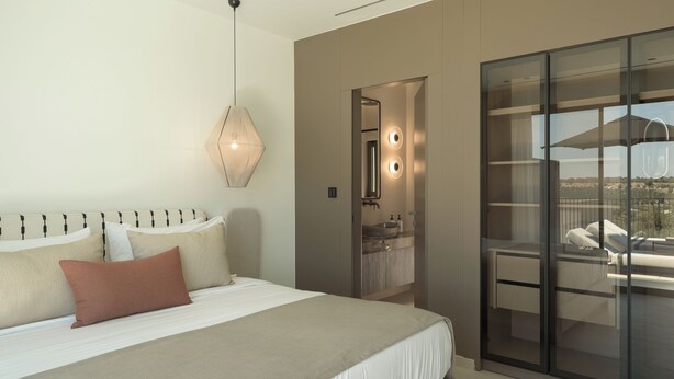 Une chambre moderne avec un lit, un luminaire suspendu, une salle de bain avec une porte en verre et un balcon avec vue.