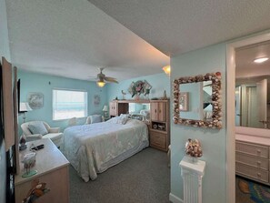 Ein Schlafzimmer mit einem Bett, einem Schreibtisch, einem Stuhl, einer Kommode, einem Spiegel und einem Deckenventilator.