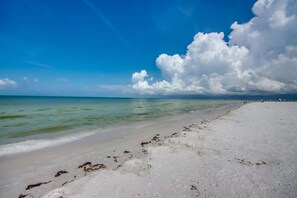 Ein Strand mit klarem Wasser, sandigem Ufer und einem teils bewölkten Himmel.