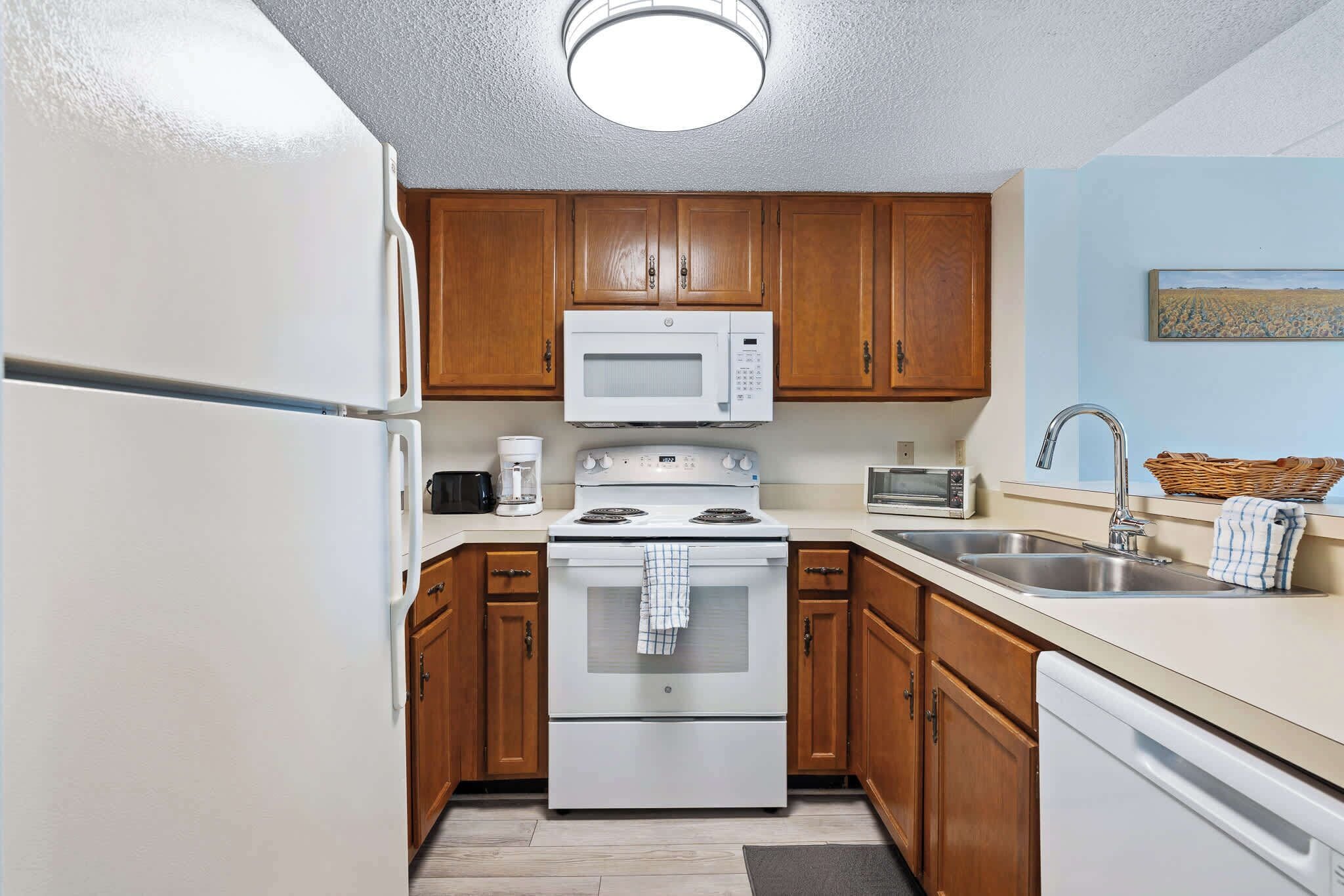 A compact kitchen with wooden cabinets, a white refrigerator, a microwave, a stove, and a dishwasher.